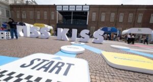 Kiss Kiss Way 2025: Villaggio con palco, stand brand e pubblico festante durante una tappa estiva del tour